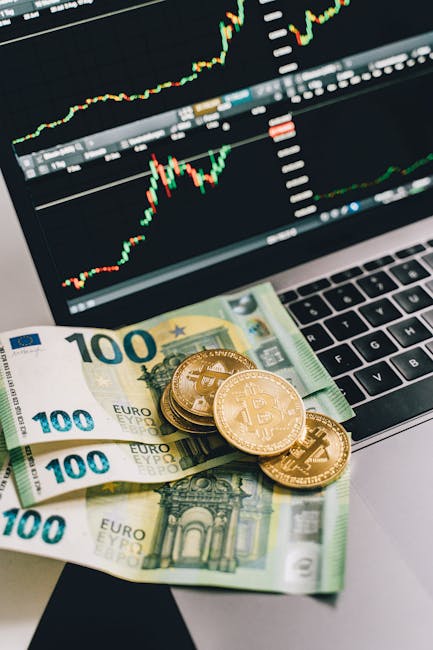 Bitcoin coins and Euro notes on a laptop with a stock market graph display, symbolizing modern finance.